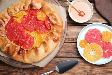 Photo of Tasty galette with citrus fruits served on wooden table, flat lay