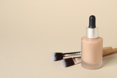 Bottle of skin foundation and brushes on beige background, space for text. Makeup product