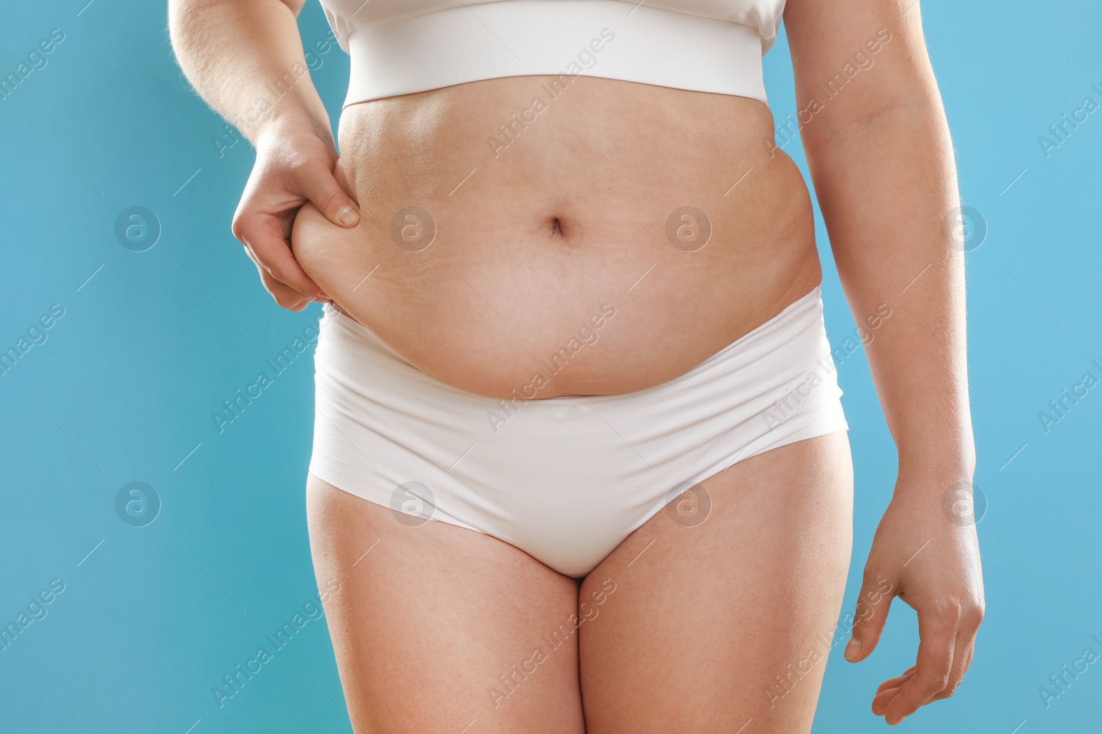 Photo of Woman touching belly fat on light blue background, closeup. Overweight problem