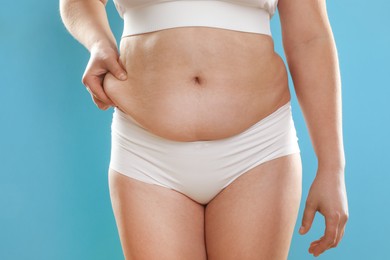 Photo of Woman touching belly fat on light blue background, closeup. Overweight problem