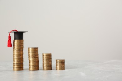 Photo of Scholarship concept. Graduation cap and stacked coins on light grey table, space for text