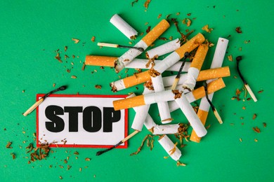 Photo of Stop smoking concept. Card with word Stop, cigarette stubs, tobacco and burnt matches on green background, flat lay