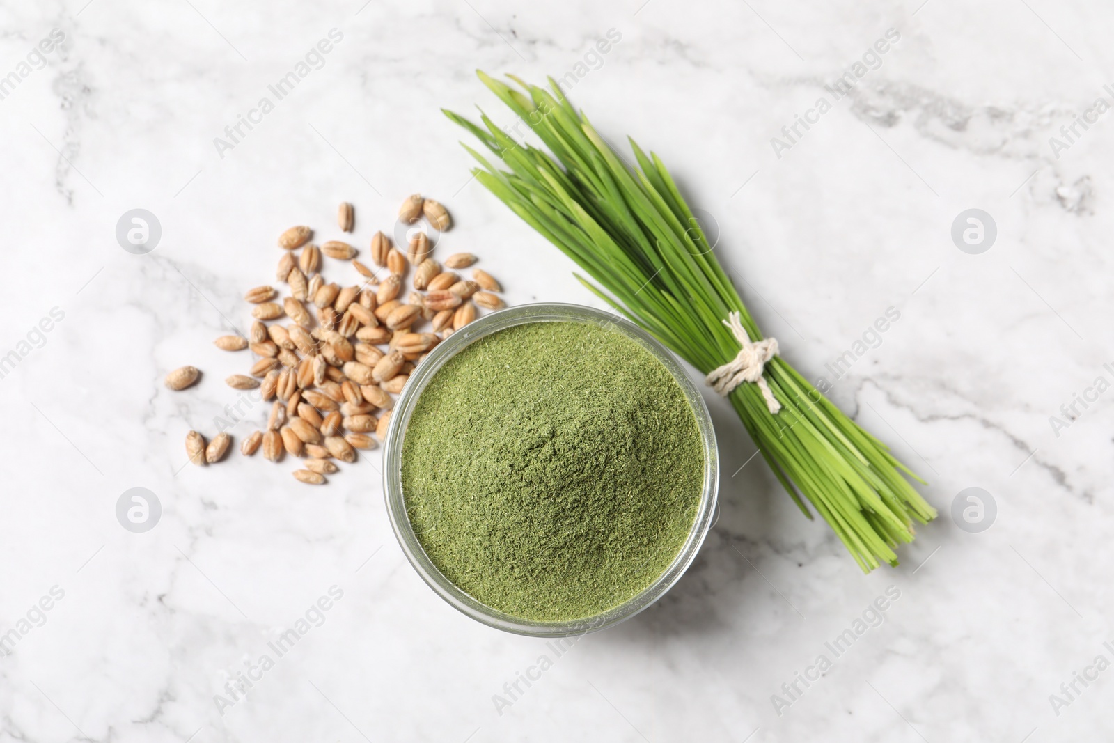 Photo of Wheat grass powder in bowl, seeds and fresh sprouts on white marble table, flat lay