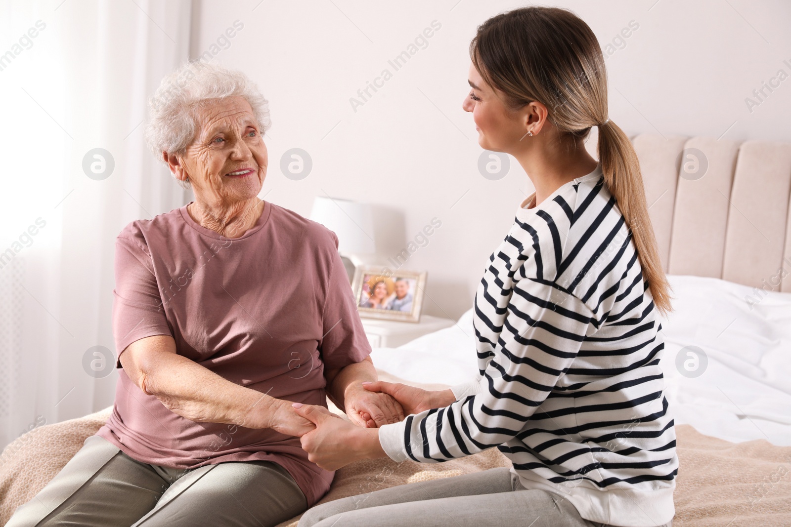 Photo of Young caregiver talking to senior woman in bedroom. Home care service