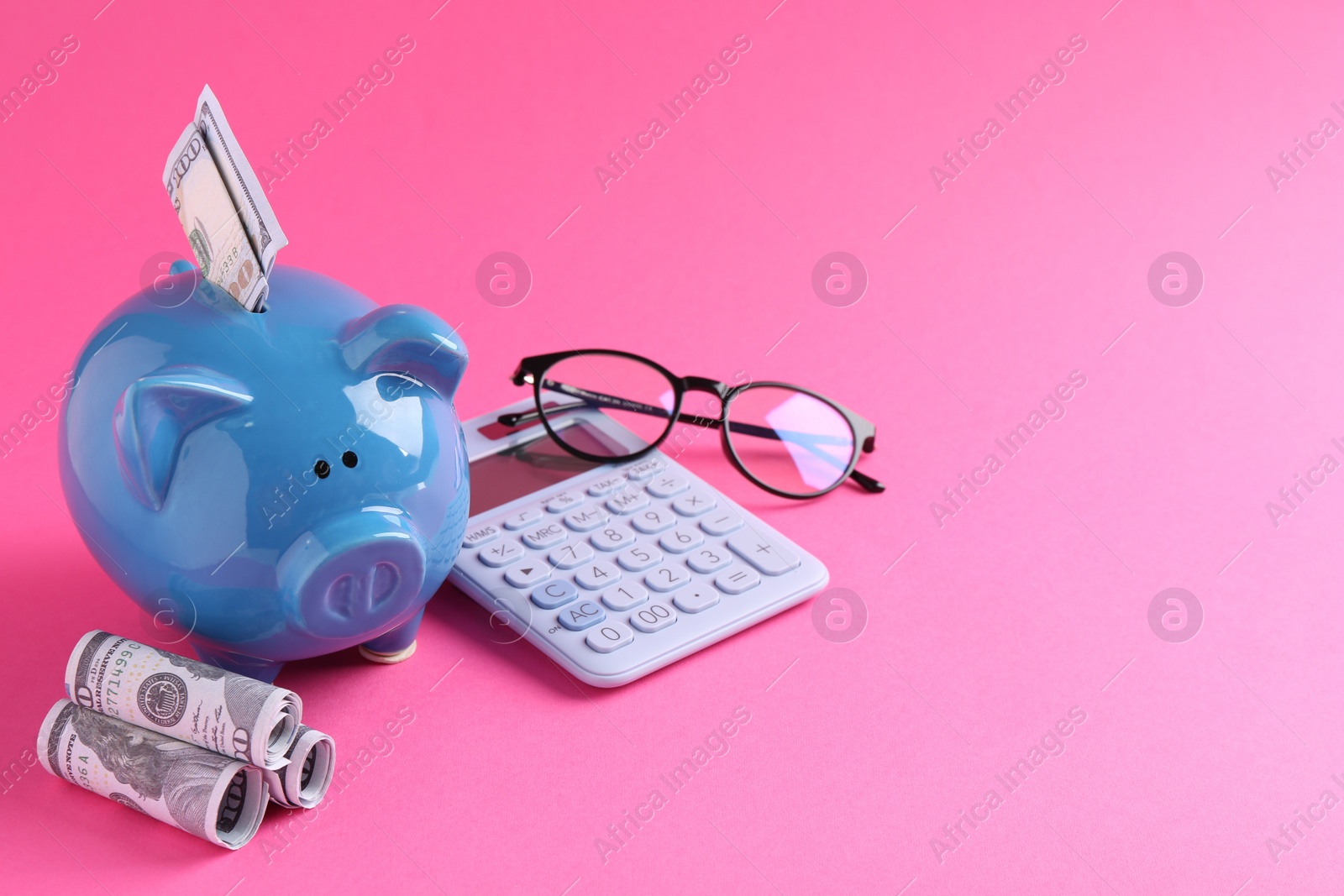 Photo of Financial savings. Piggy bank, dollar banknotes, glasses and calculator on pink background, space for text