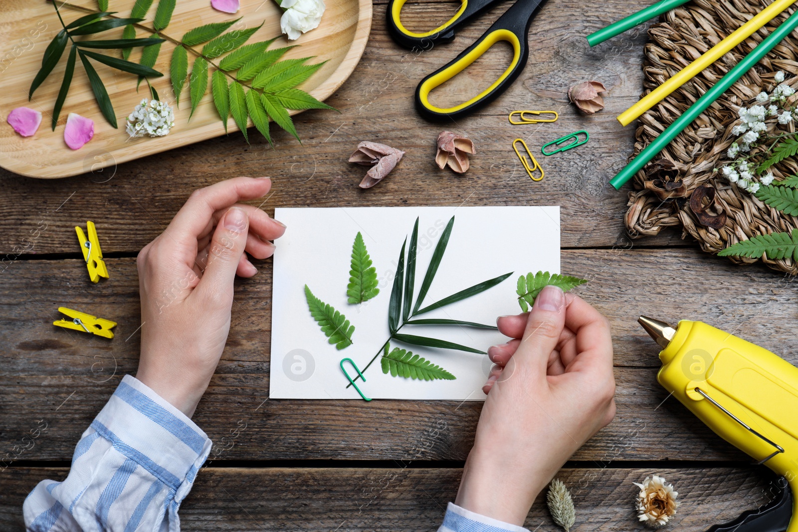 Photo of Woman with card and plant leaf at wooden table, top view. Master class in handmade craft