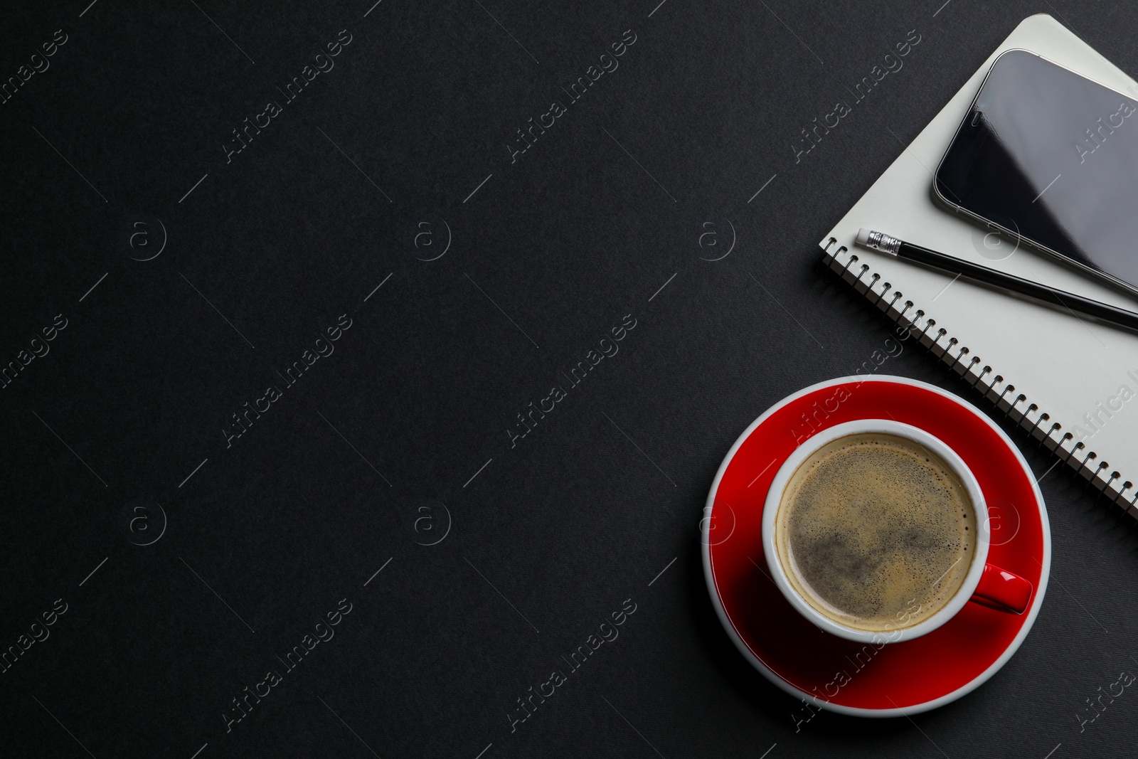 Photo of Red ceramic cup with hot aromatic coffee , notebook and smartphone on black background, flat lay. Space for text