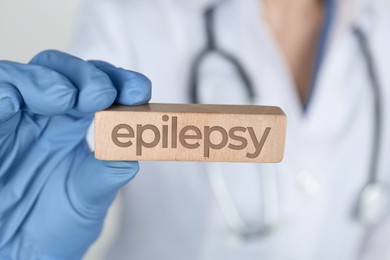 Photo of Doctor holding wooden block with word Epilepsy on light grey background, closeup
