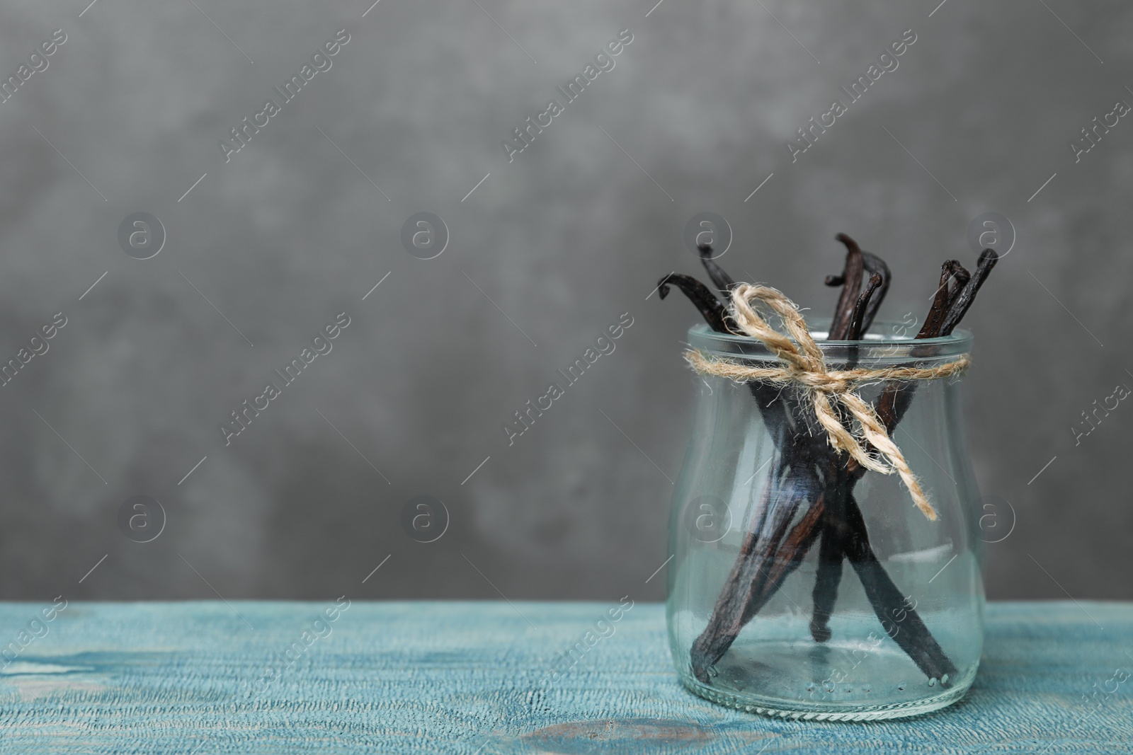 Photo of Jar with vanilla sticks on wooden table against grey background