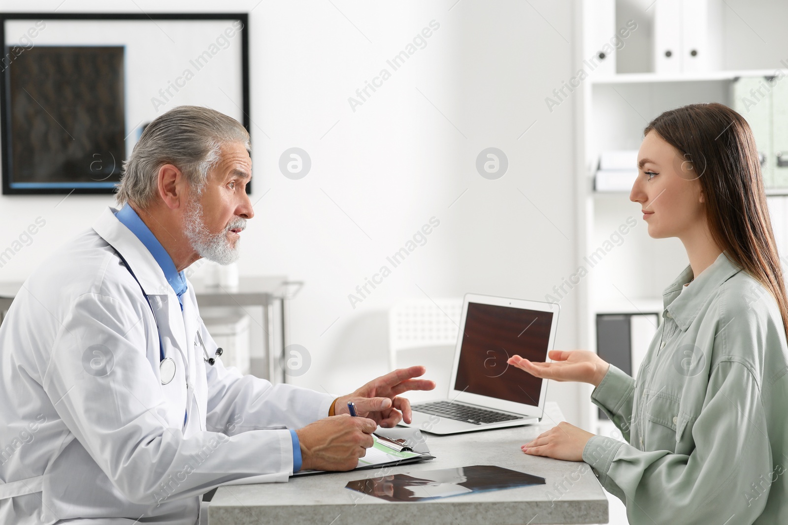 Photo of Professional orthopedist consulting patient at table in clinic