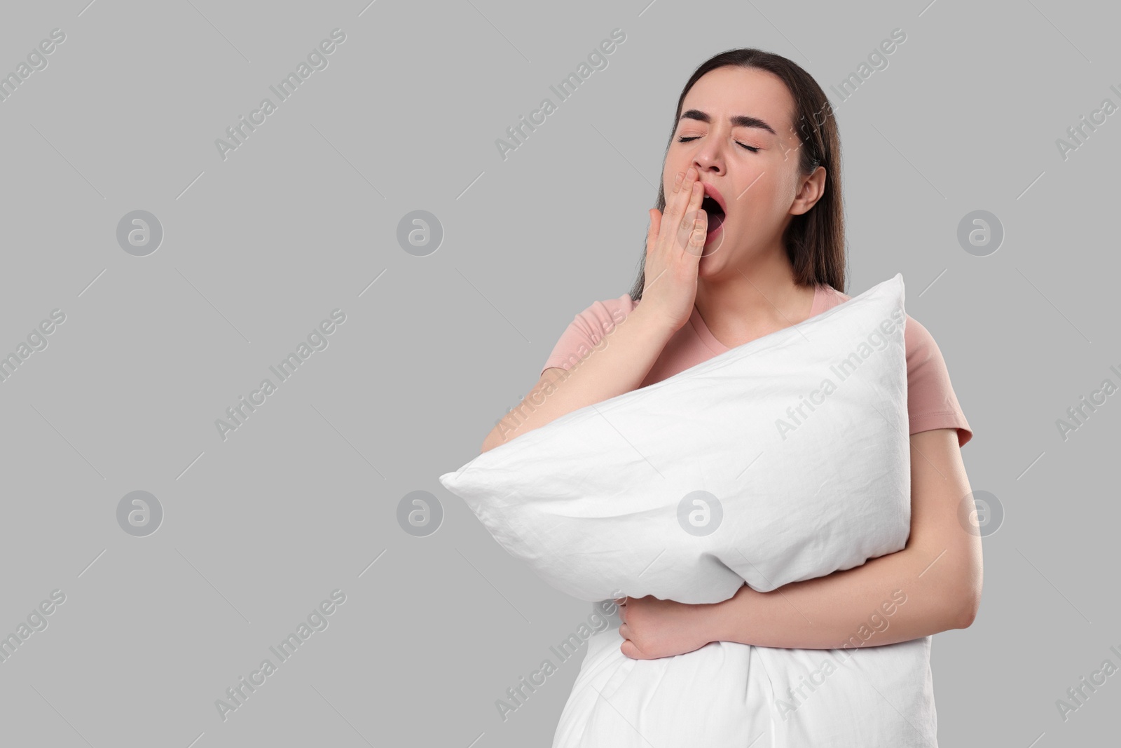 Photo of Tired young woman with pillow yawning on light grey background, space for text. Insomnia problem