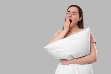Tired young woman with pillow yawning on light grey background, space for text. Insomnia problem