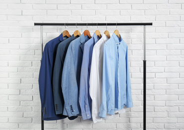 Rack with stylish men's clothes near white brick wall