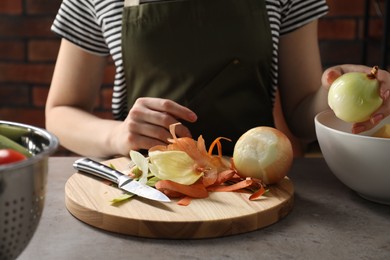 Photo of Woman with fresh onion and peels of vegetables at grey table indoors, closeup