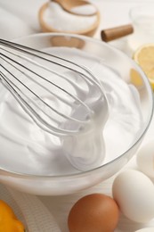 Photo of Bowl with whipped cream, whisk and ingredients on white wooden table, closeup