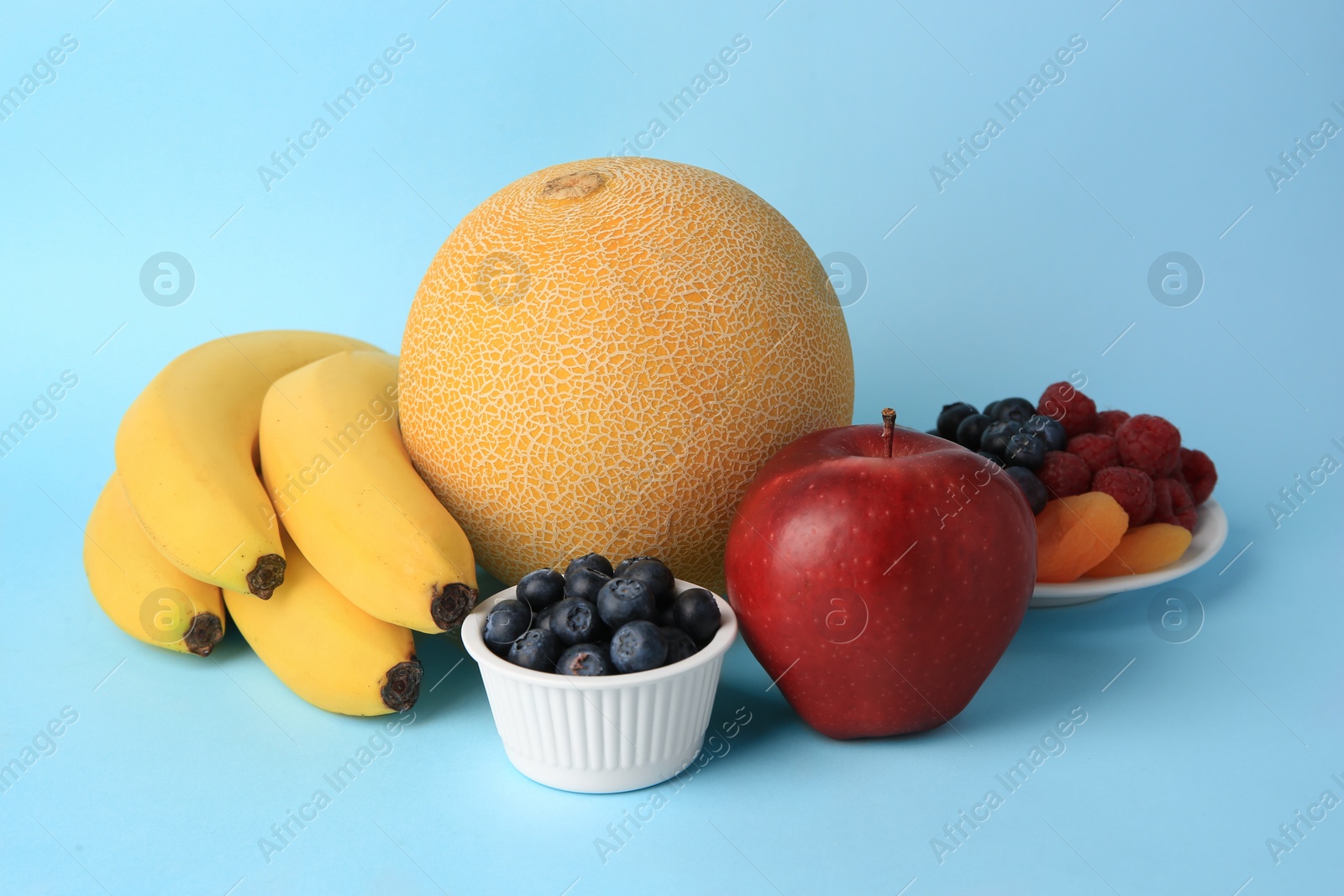 Photo of Delicious ripe fruits, berries and dried apricots on light blue background