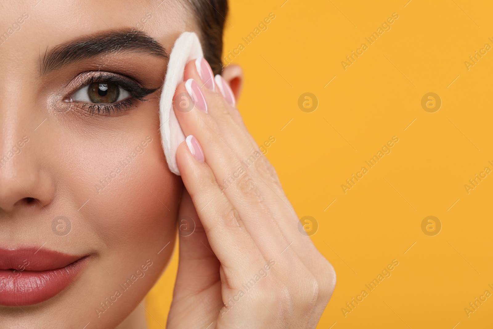 Photo of Beautiful woman removing makeup with cotton pad on orange background, closeup. Space for text