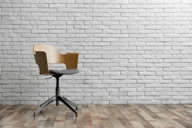 Comfortable office chair near white brick wall indoors. Space for text