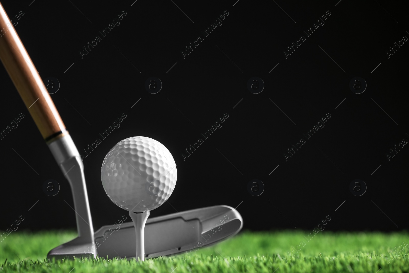 Photo of Hitting golf ball with club on artificial grass against black background, space for text