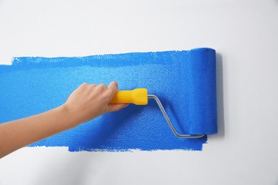 Photo of Woman painting white wall with blue dye, closeup. Interior renovation