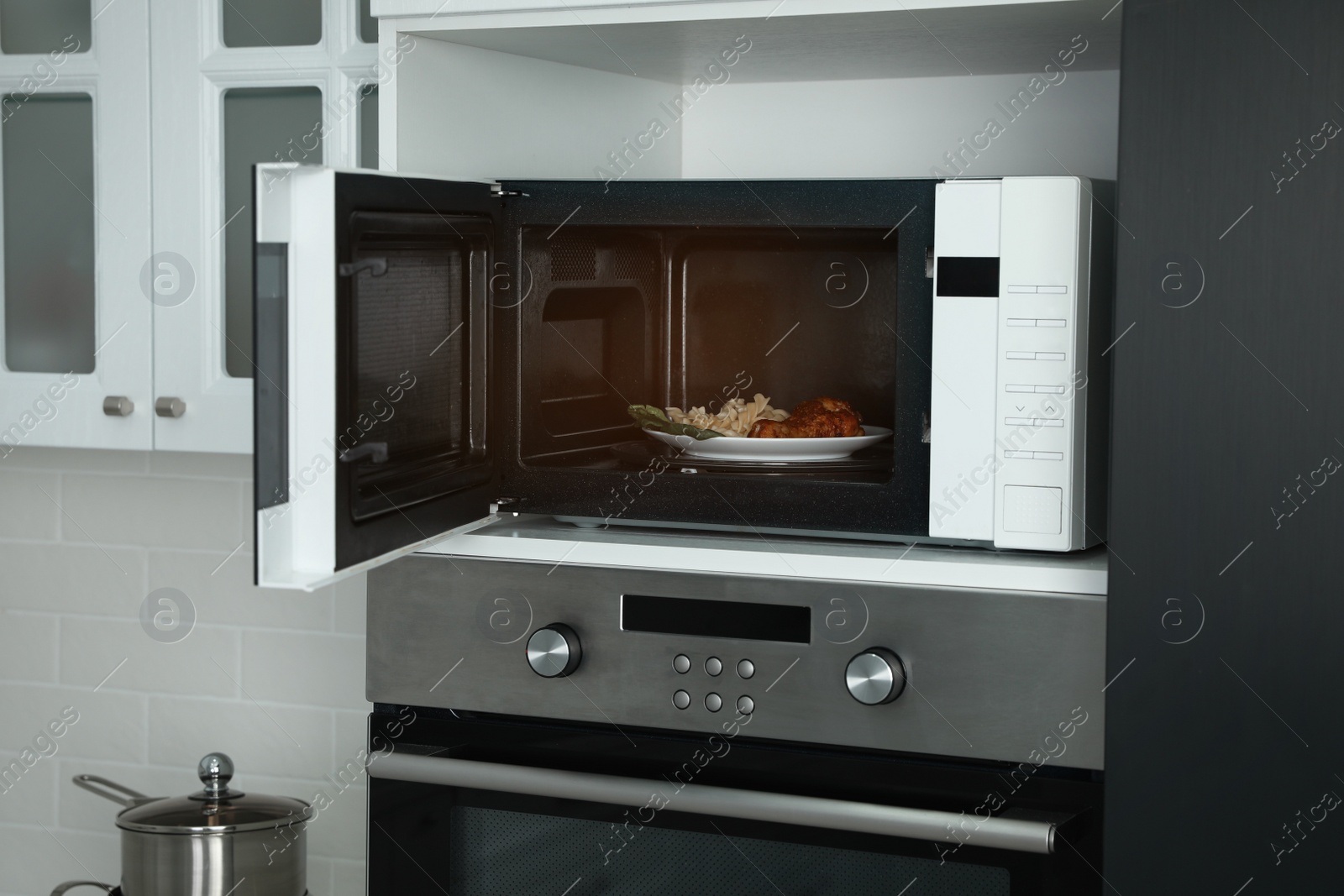 Photo of Open microwave oven with food on white shelf in kitchen