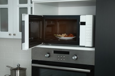 Photo of Open microwave oven with food on white shelf in kitchen