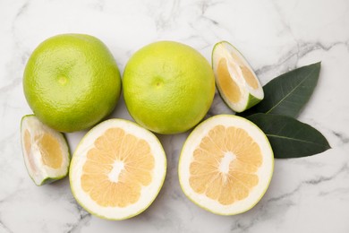 Photo of Whole and cut sweetie fruits with green leaves on white marble table, flat lay