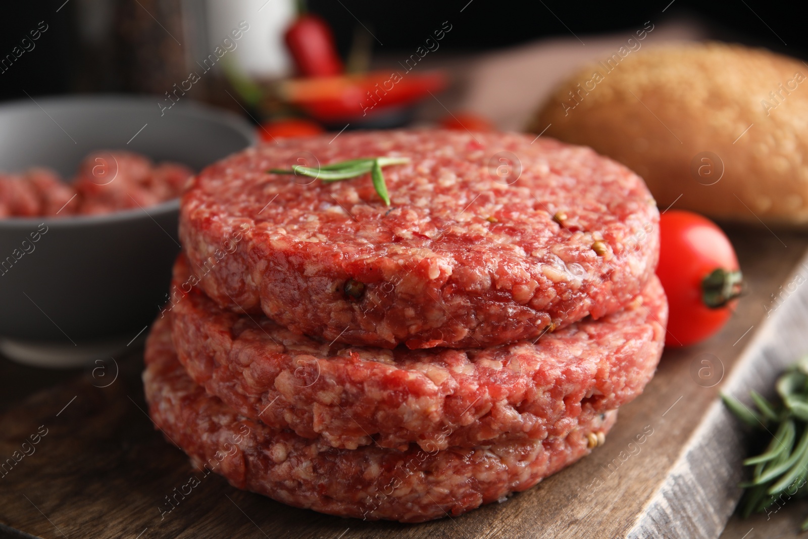 Photo of Raw hamburger patties with rosemary on wooden board, closeup