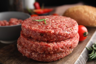 Photo of Raw hamburger patties with rosemary on wooden board, closeup