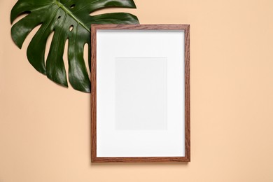 Photo of Empty photo frame and green leaf on beige background, flat lay. Space for design