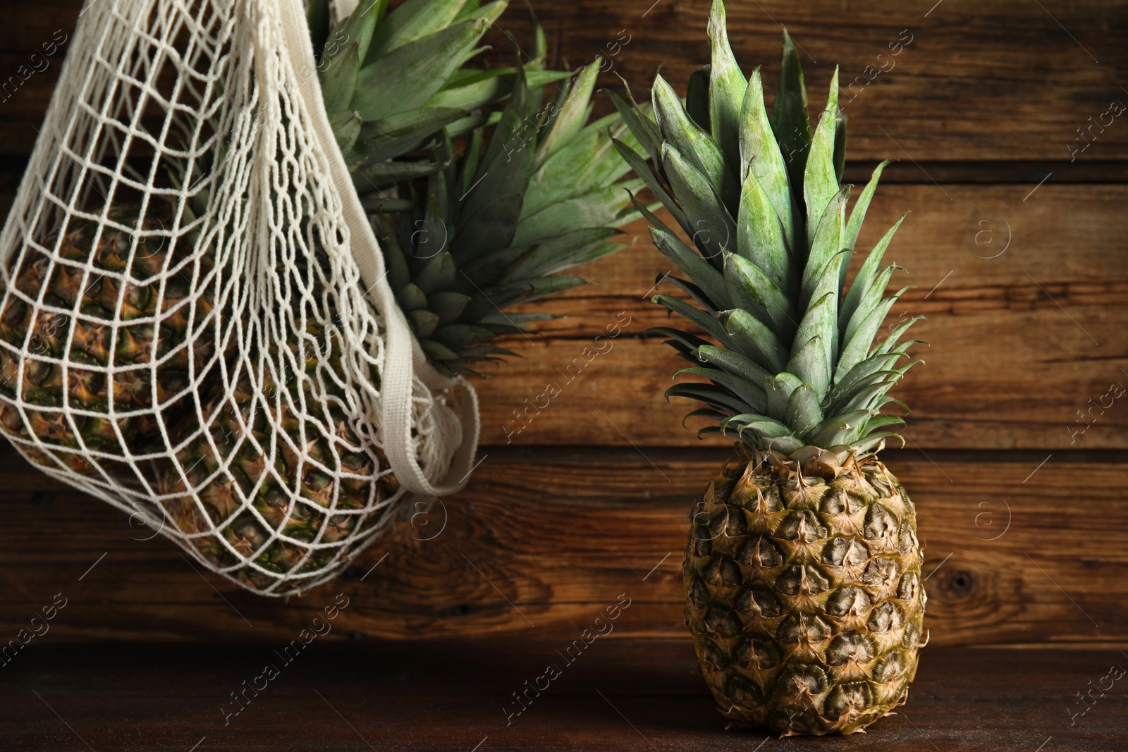 Photo of Bag and fresh juicy pineapples on wooden background