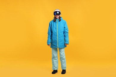 Photo of Winter sports. Happy woman with snowboard goggles on orange background