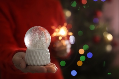 Photo of Woman holding snow globe on blurred background, closeup. Space for text