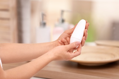 Young woman holding deodorant in bathroom, closeup