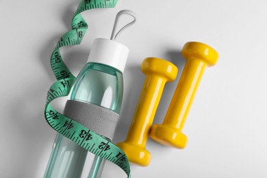 Measuring tape, dumbbells and bottle with water on white background, flat lay. Weight control concept