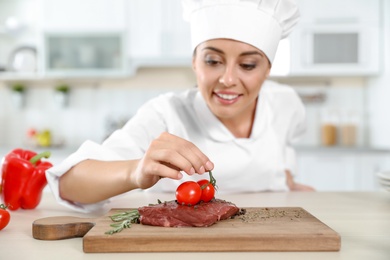 Professional female chef cooking meat on table in kitchen