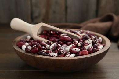 Photo of Bowl with dry kidney beans and scoop on wooden table, closeup