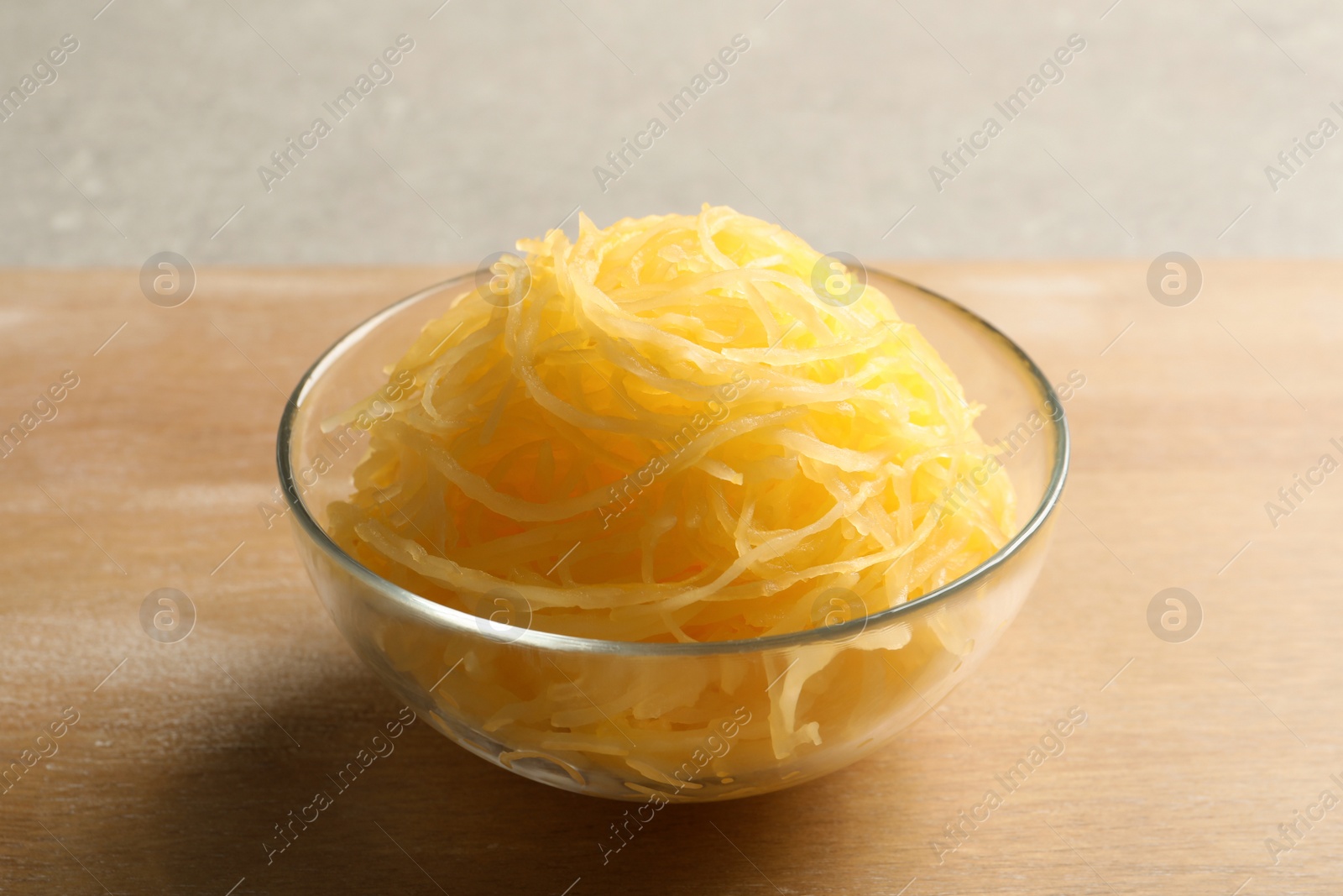 Photo of Bowl with cooked spaghetti squash on wooden board