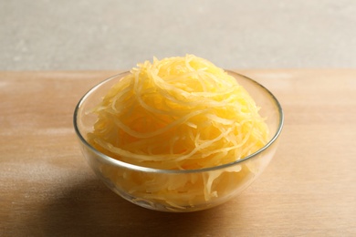 Bowl with cooked spaghetti squash on wooden board