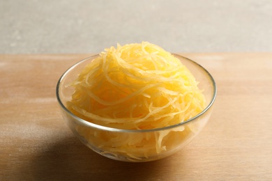 Photo of Bowl with cooked spaghetti squash on wooden board