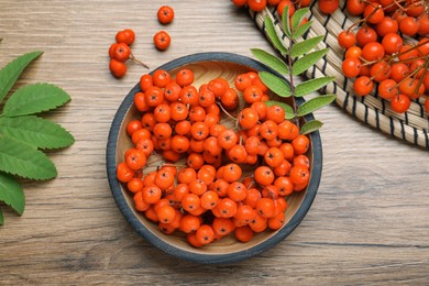 Photo of Fresh ripe rowan berries and leaves on wooden table, flat lay