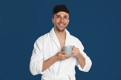 Photo of Young man in bathrobe with cup of coffee on blue background