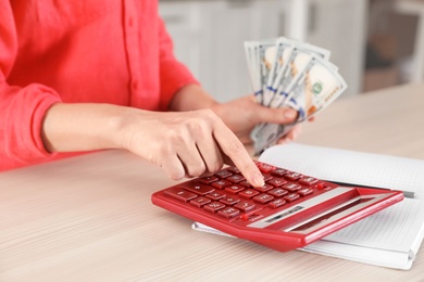 Photo of Woman counting money with calculator at table, closeup