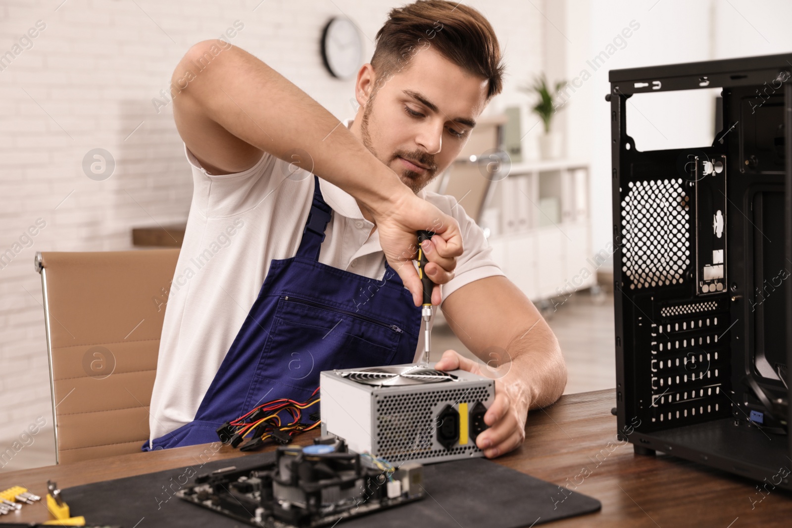 Photo of Male technician repairing power supply unit at table indoors