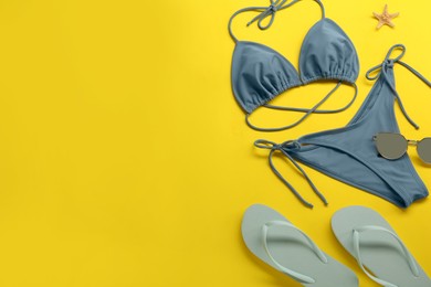 Photo of Stylish blue bikini, sunglasses and flip flops on yellow background, flat lay. Space for text