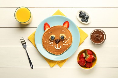 Photo of Creative serving for kids. Plate with cute cat made of pancakes, berries, cream, banana and chocolate paste on white wooden table, flat lay