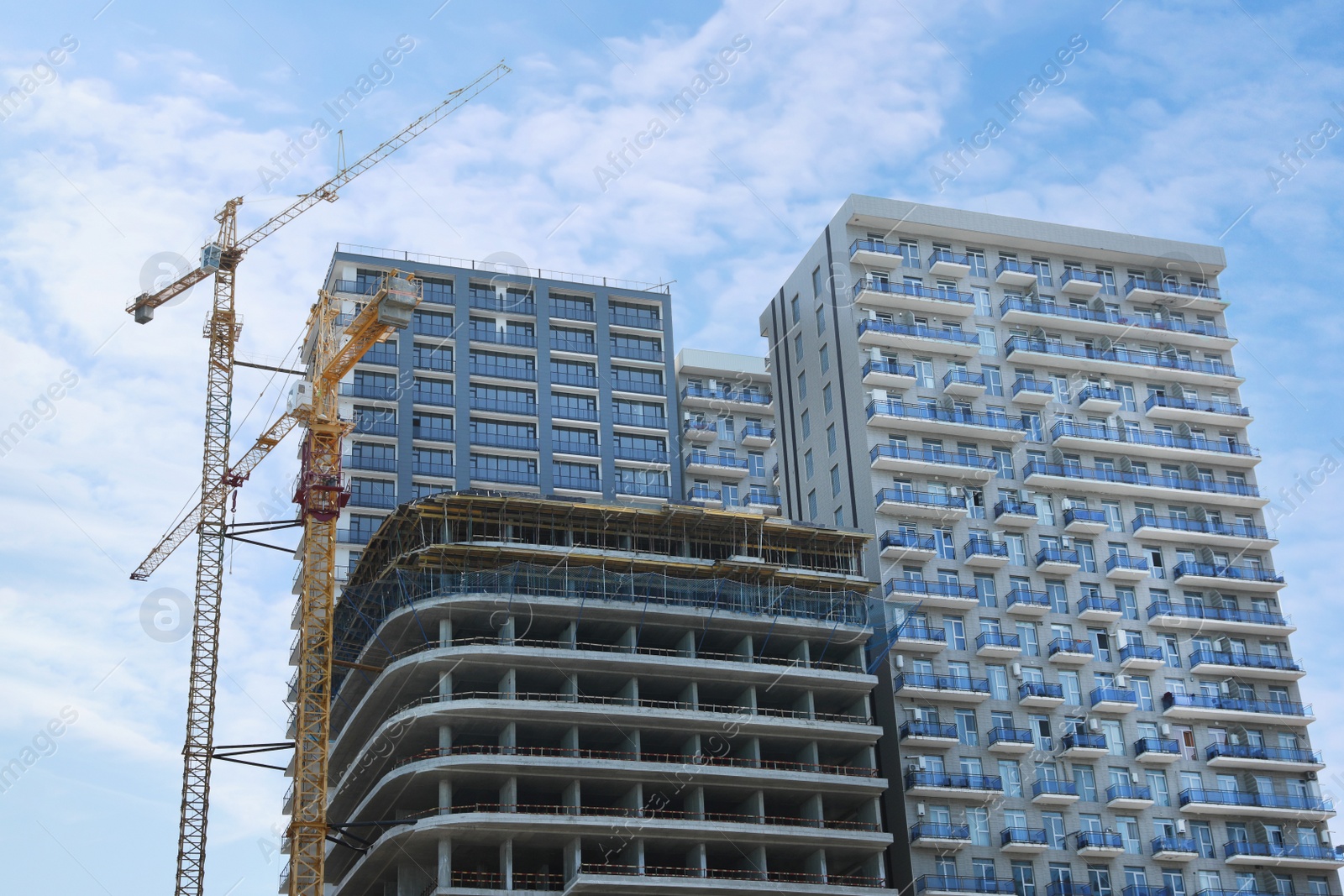 Photo of Construction site with tower cranes near unfinished building, low angle view