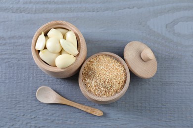 Photo of Dehydrated garlic granules, peeled cloves and spoon on grey wooden table, flat lay