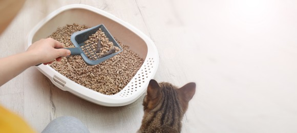 Image of Woman cleaning cat litter tray at home, closeup. Banner design with space for text