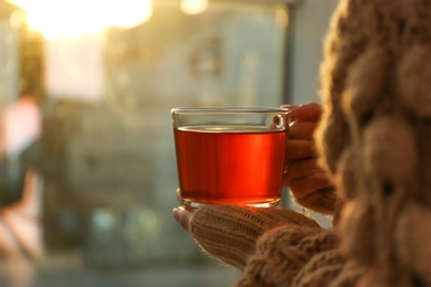 Photo of Woman holding glass cup of tea indoors, closeup
